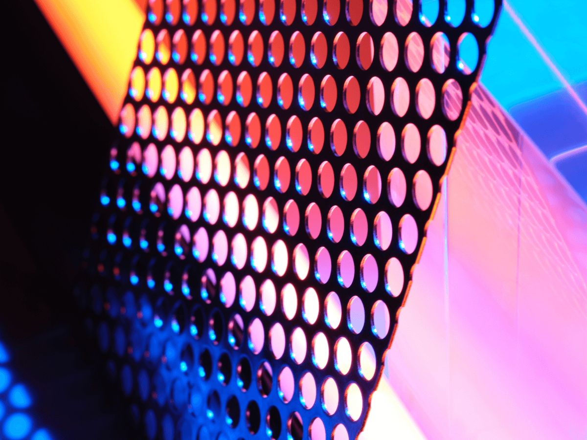 An abstract image featuring a perforated grid or mesh illuminated by vibrant blue, pink, orange, and purple lighting, representing technology or data flow, suitable for non-relational database themes.