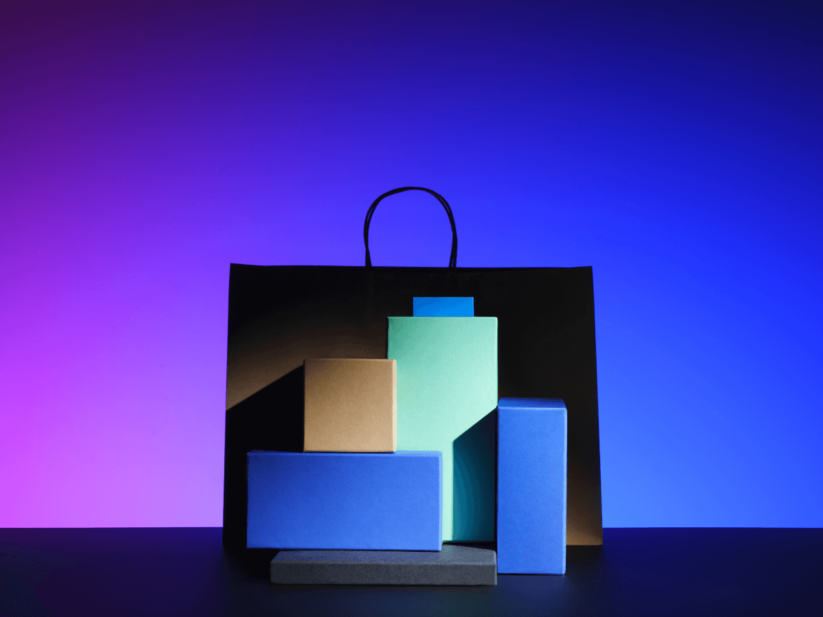 A black shopping bag with colorful rectangular boxes arranged in front, set against a vibrant blue and purple gradient background.