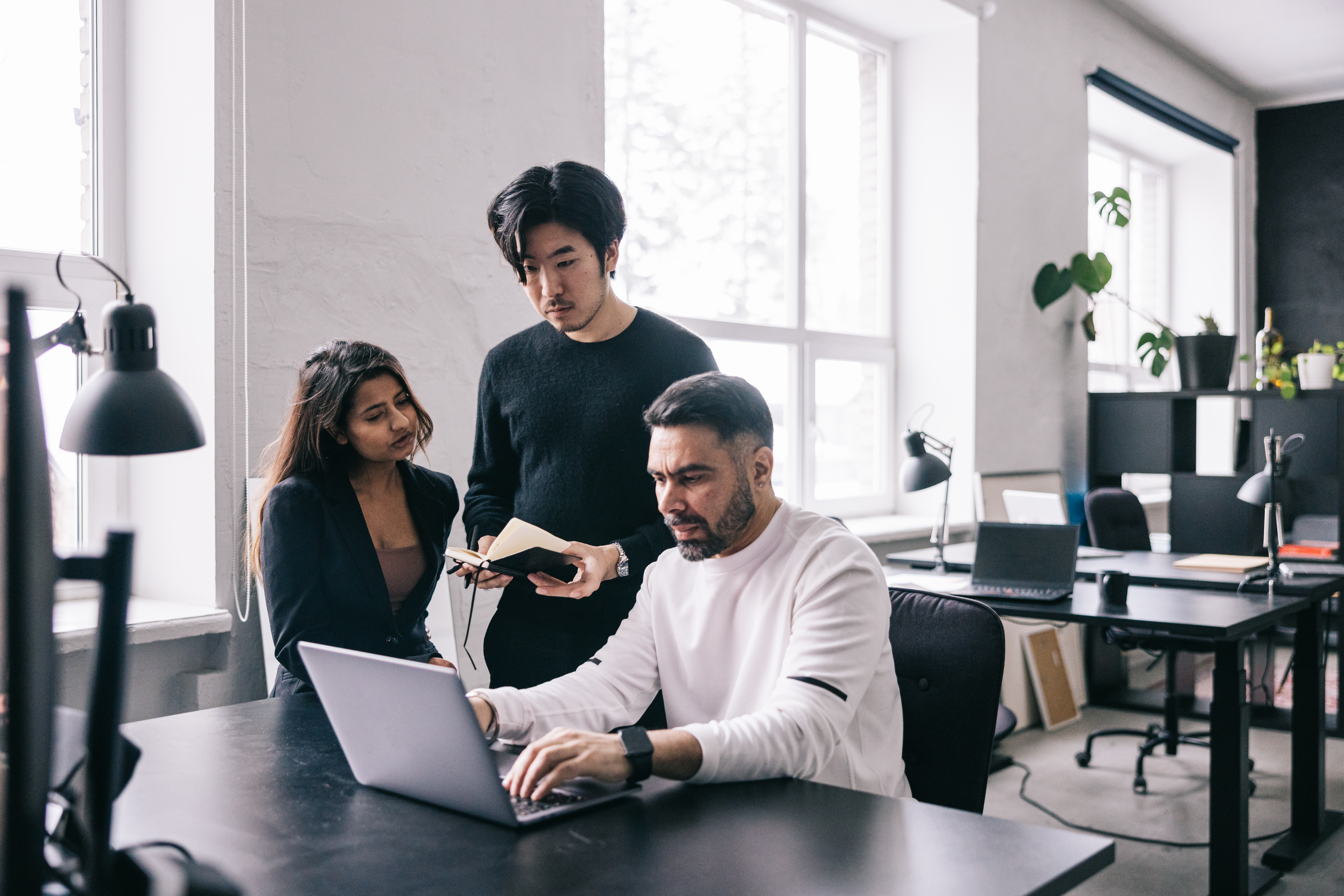 Three colleagues collaborating around a laptop in a bright, modern office, representing teamwork and workplace collaboration.