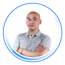 Portrait of a person wearing a grey polo shirt, arms crossed, standing in front of a white background, inside a blue circular graphic frame.