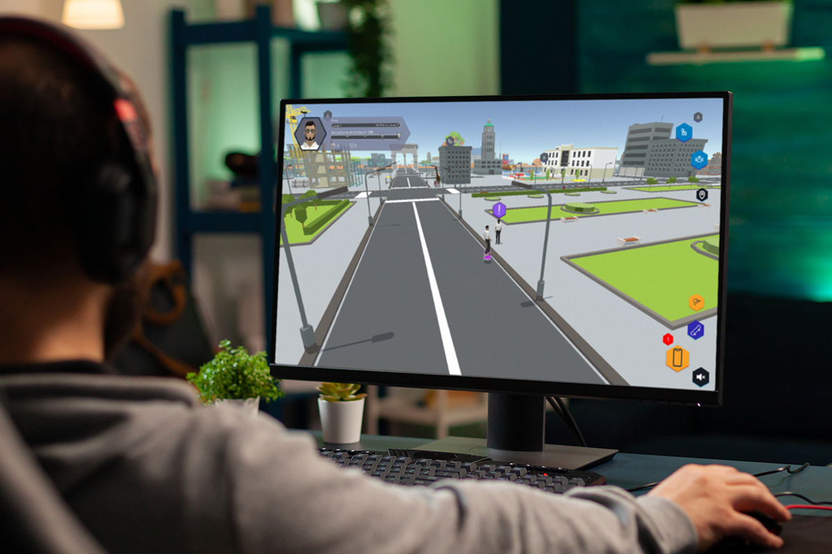 A person wearing headphones is playing AWS Cloud Quest, a cloud learning game, on a computer in a modern home environment. The monitor displays a virtual cityscape interface from the game.